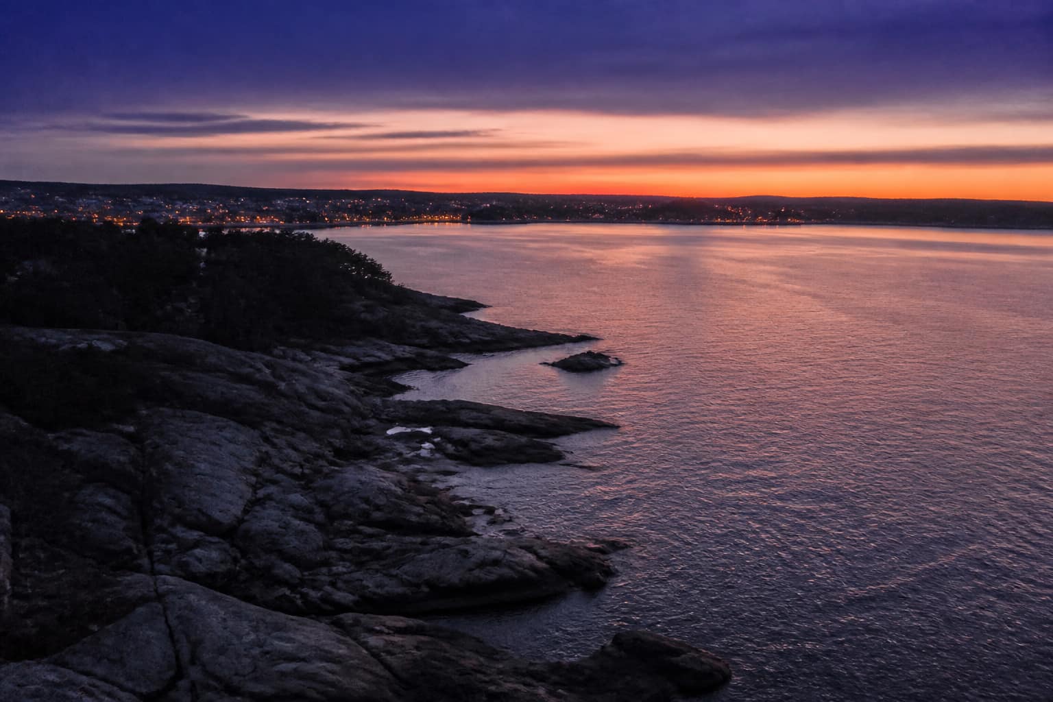 Coastal shoreline at dusk with distant lights beginning to glow